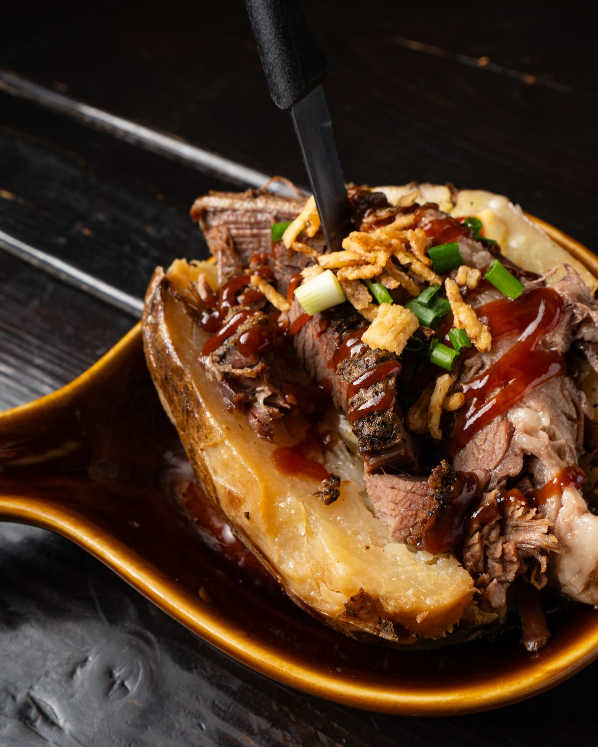 Smoked brisket piled on a loaded baked potato with BBQ sauce and crispy onions