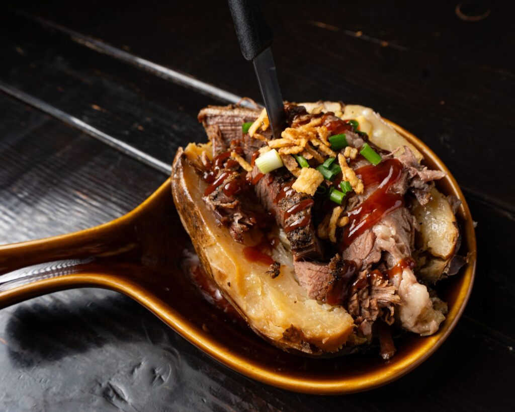 Sliced smoked brisket on a loaded baked potato with BBQ sauce and crispy onions