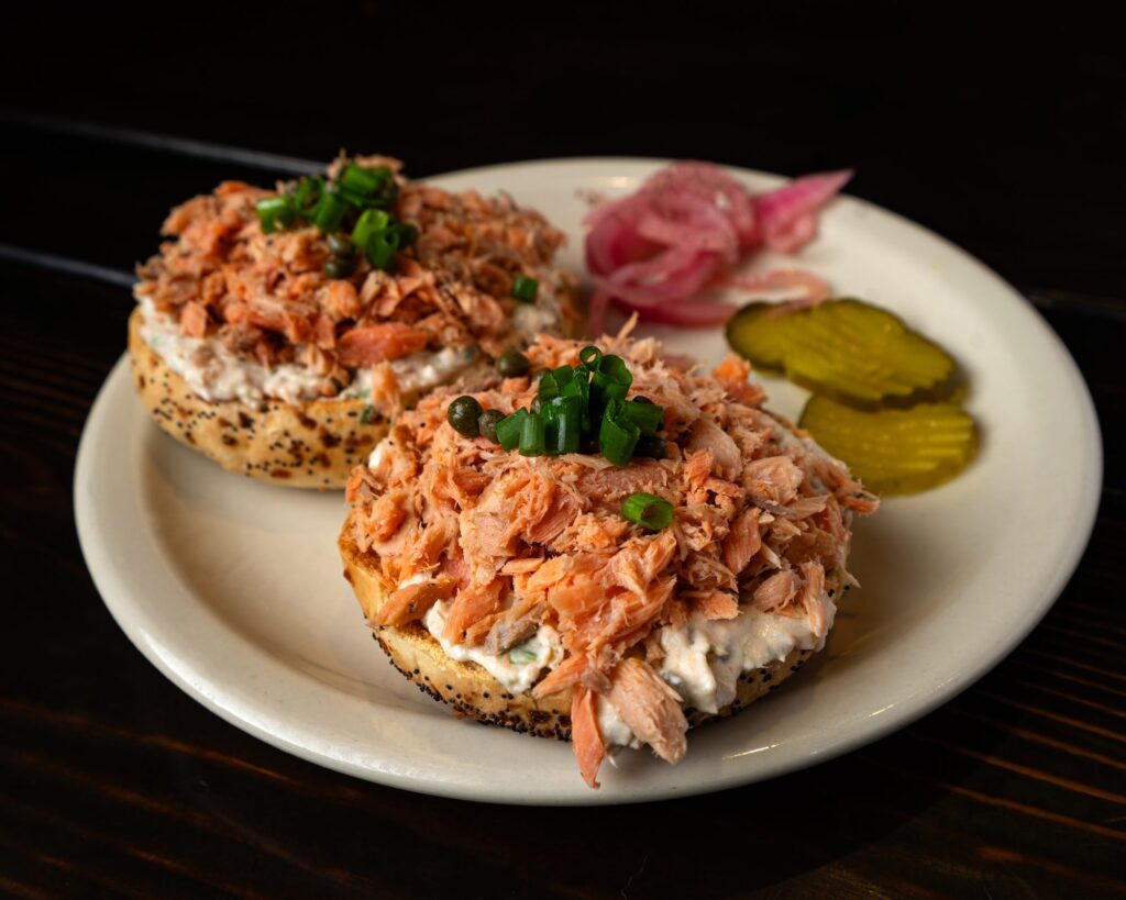 Smoked salmon piled on a toasted bagel with cream cheese, pickles and pickled onion
