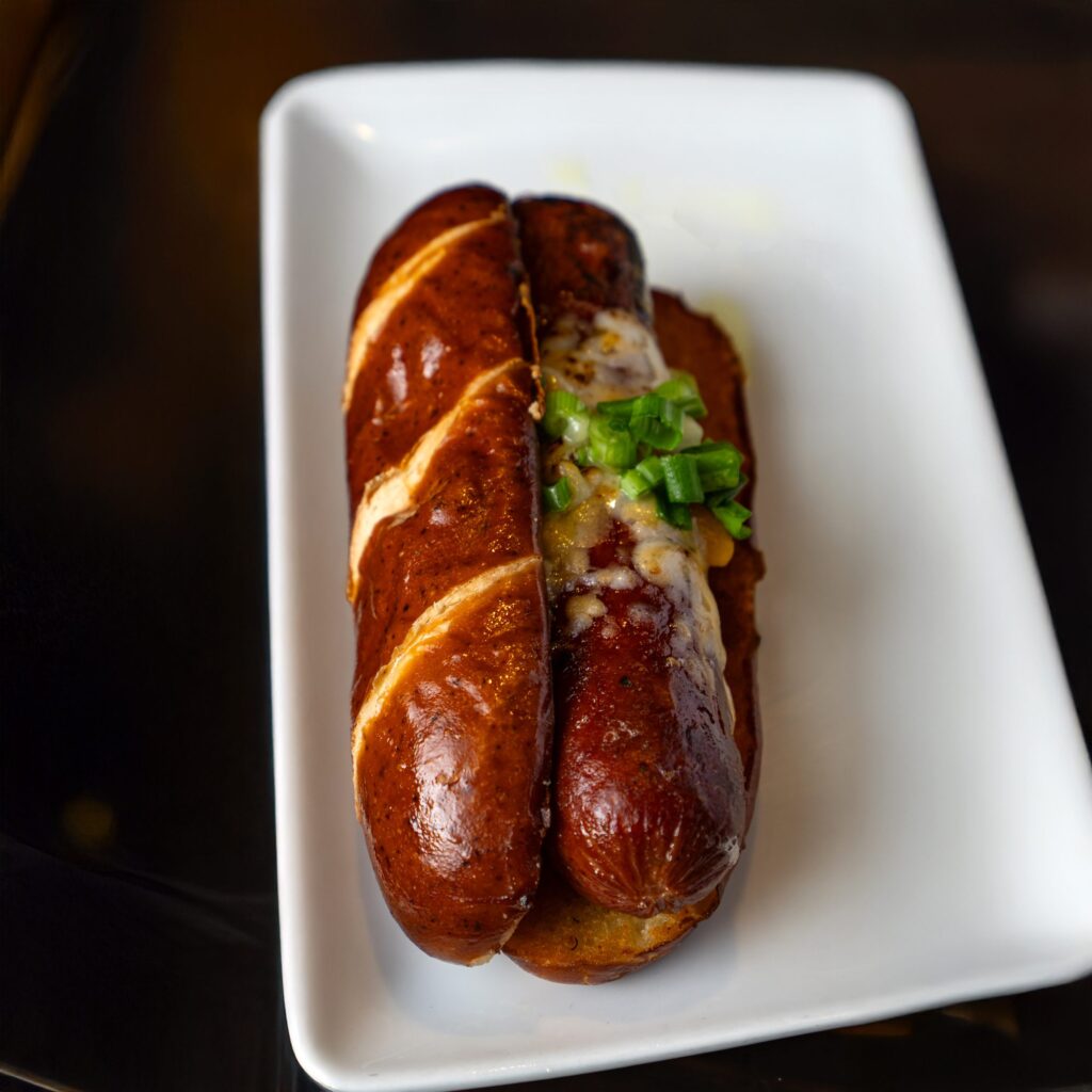 Smoked sausage in a pretzel bun topped with cheese and green onion